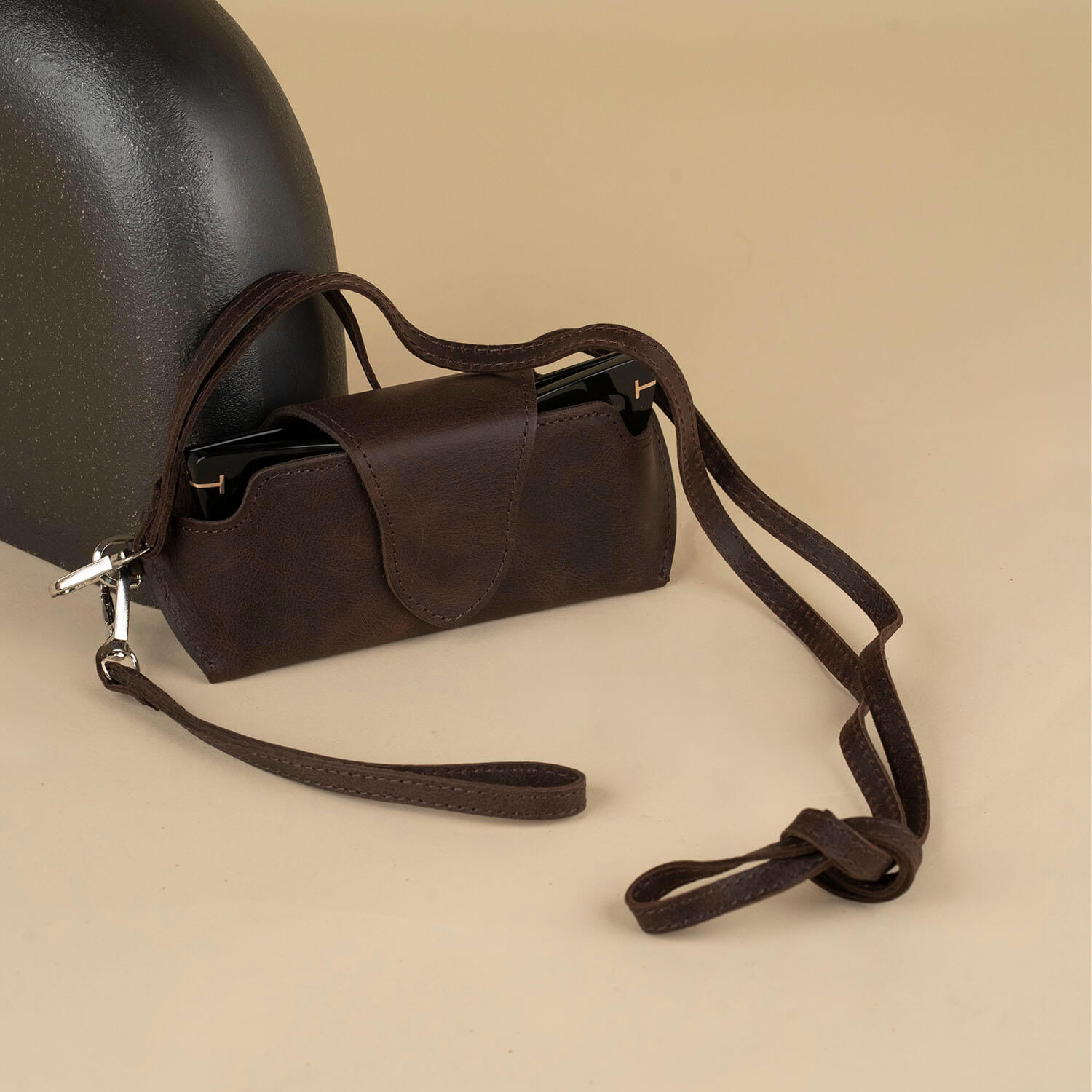 Dark brown leather sunglass case with wrist strap by LEATHERE, designed for eyewear accessories, shown with open and closed views.